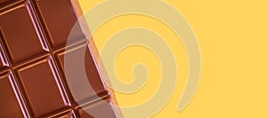 A bar of milk chocolate closeup on a yellow background.