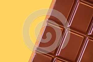 A bar of milk chocolate closeup on a yellow background.