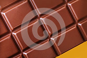 A bar of milk chocolate closeup on a yellow background.