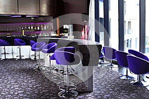 Bar with purple bar stools and large windows. Bar counter. Bottles on the shelf