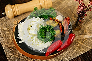 Bar snacks portion on wooden board: cecil cheese, hot peppers, olives, sun-dried tomatoes, fresh parsley leaves.