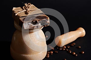 A bar of soap or body scrub on beige marble mortar, isolated on black background with scattered coffee beans and pestle