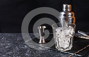 Bar tools for making cocktail. Shaker and a glass of ice on dark stone table.