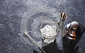 Bar tools for making cocktail. Shaker and a glass of ice on dark stone table.