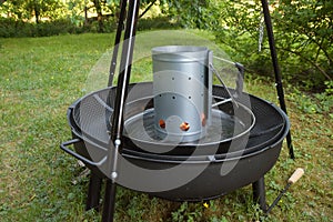 Barbecue charcoal chimney starter on a black tripod swivel grill photo