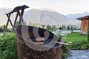 Barbecue with charcoal, sausages and meat in front of alpine mountain panorama view in Salzburgerland, Austria
