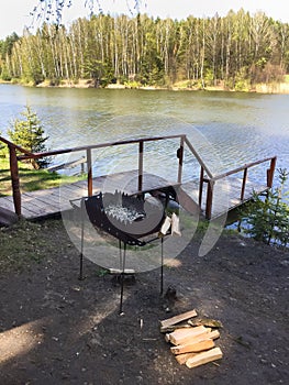 Barbecue for cooking meat in nature, firewood, pier, down to the lake water.