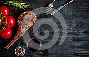 Barbecue dry aged rib of beef with spice, vegetables and glass of red wine close-up on black wooden background