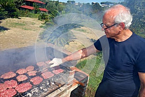 Anziani abile uomo per cucinare la carne su una griglia per BARBECUE all'aperto.