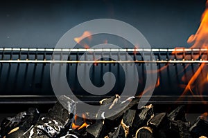 Barbecue grill pit with glowing and flaming hot open fire with red flame, hot charcoal briquettes and embers