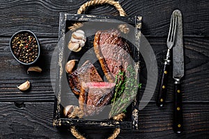 Barbecue Grilled rump cap or brazilian picanha beef meat steak in a wooden tray. Black wooden background. Top view