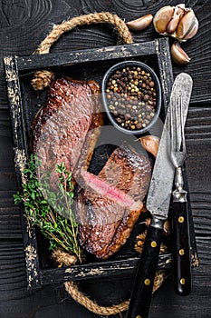 Barbecue Grilled rump cap or brazilian picanha beef meat steak in a wooden tray. Black wooden background. Top view