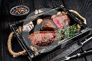 Barbecue Grilled rump cap or brazilian picanha beef meat steak in a wooden tray. Black wooden background. Top view