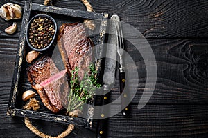 Barbecue Grilled rump cap or brazilian picanha beef meat steak in a wooden tray. Black wooden background. Top view. Copy