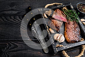 Barbecue Grilled rump cap or brazilian picanha beef meat steak in a wooden tray. Black wooden background. Top view. Copy space