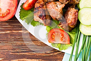 Barbecue on a plate, greens and vegetables on a wooden table