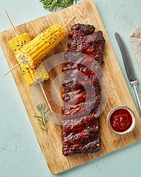 Barbecue pork ribs. Slow cooking recipe. Whole pickled roasted pork meat with red sauce and corn on cutting board