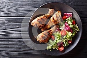 Barbecue serving of grilled chicken drumsticks and fresh vegetable salad closeup. Horizontal top view