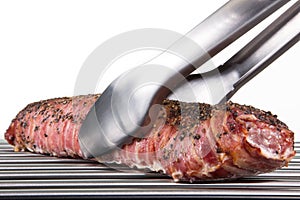 Barbecue tongs grabs a big portion of roast pork, isolated on white.