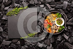 Barbecue vegetables in a frying pan and a cutting stone board on coals.