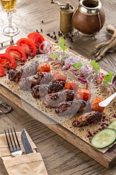 Barbecued kofta kebeb with onion and fresh tomato on lavash bread on wooden table