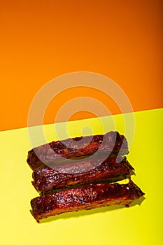Barbecued and marinated sticky spare rib on yellow and orange background with copy space.