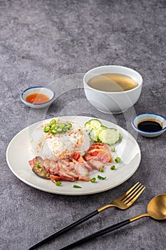 Barbecued red pork in sauce with rice on a white plate, accompanied by soup and dipping sauce, is presented elegantly