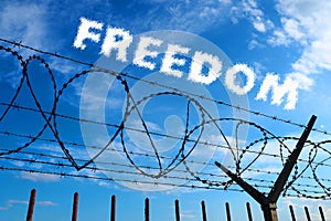 Barbed wire against the blue sky and white clouds. The inscription is blurred in white - freedom. The concept of freedom