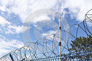 Barbed wire against cloudy sky, close-up. Metal fence with barbed wire,