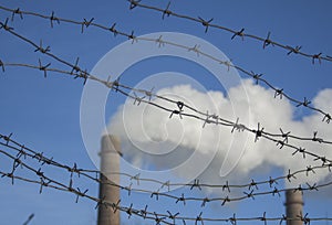 Barbed wire bottom view against a blue sky and smoking pipes. Environmental problems, ecological theme