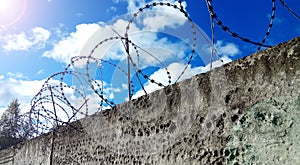 Barbed wire on a dark fence. Against a blue sky with clouds.