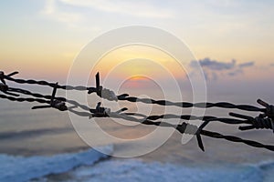 Barbed wire fence against sunset sky and sea