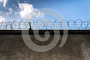 Barbed wire fence around prison walls, blue cloudy sky in background, security, crime illegal immigration concept