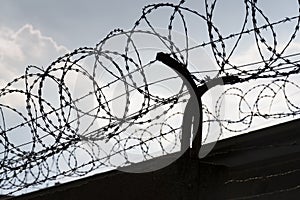 Barbed wire fence around prison walls blue sky