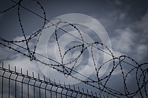 Barbed wire fence in dark colors on background with dark sky. Metaphor concept of prison, jail, arrest. Prohibbited