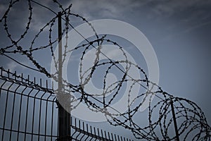 Barbed wire fence in dark colors on background with dark sky. Metaphor concept of prison, jail, arrest. Prohibbited
