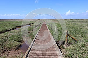 A barbed wire fence by the side of wooden walkway over Porlock salt marsh on the way back towards Bossington in Somerset, England