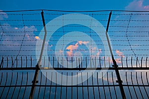 Barbed wire fence silhouettes against cloudy dark blue sky at sunset