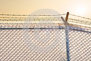 Barbed wire fence with snow at sunset.