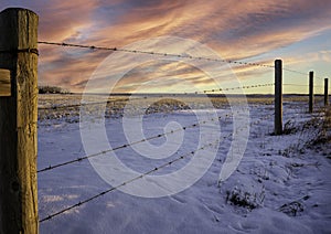 A barbed wire fence at sunrise under a dramatic sky on the Canadian prairies