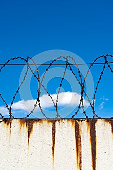 Barbed wire fence on a white wall with rust