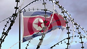Barbed wire, flag of North Korea in defocus, sky background with clouds. Concept: international sanctions, t