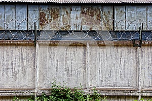 Barbed wire on a gray concrete fence and rusty building wall