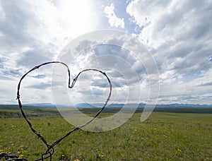 Barbed Wire Heart with Prairie and Clouds in Background