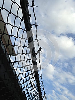 Barbed wire mesh fence against blue sky (selective focus of wire fence)