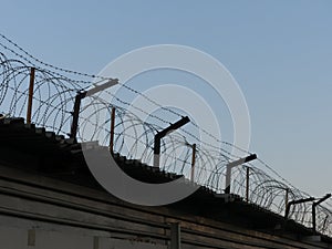 Barbed wire over a high fence against the sky