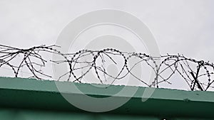 Barbed wire in prison. Jail wire with barb. Green fence with barbed wire against grey sky.