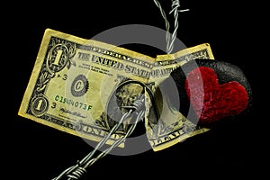 Barbed wire running through a old weathered and ripped dollar bill and a black stone with a painted red heart laying on it photo