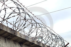 Barbed wire strung around the perimeter of a cement wall against a light sky, close-up