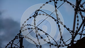 Barbed wire at the top of fence against the black, gloomy, dark sky with clouds.